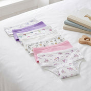 Bellabu Bear girls' bamboo underwear 7-pack laid out on a white bed: butterflies, lilac, dolphins, white, cookies and milk, pink and unicorns