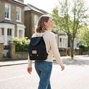Hindbag Mini Eliot backpack in black organic cotton canvas with natural straps, worn by a woman walking down a London street
